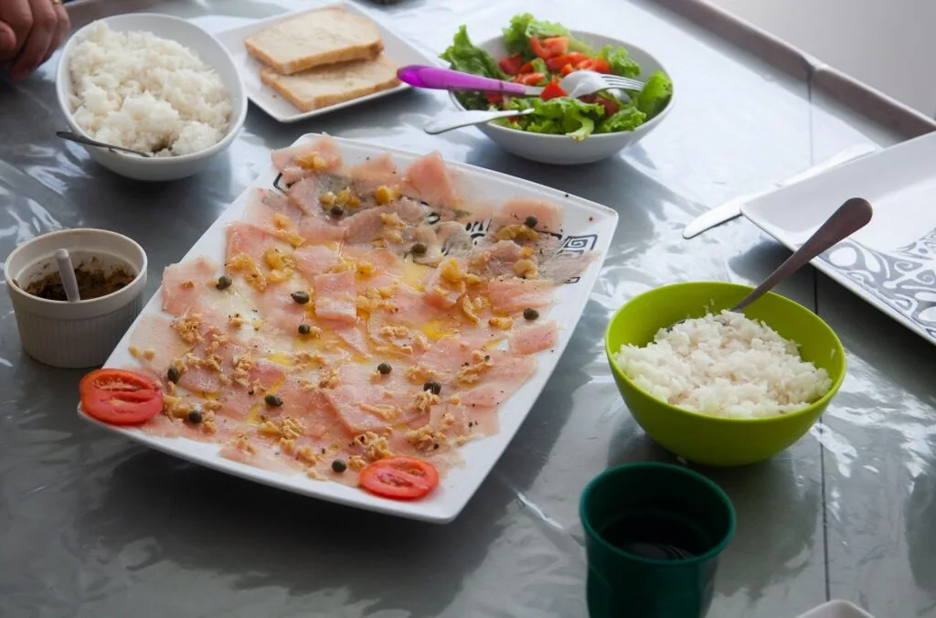 Thinly Sliced Carpaccio with Nuts and Capers on a Rectangular Plate, with Bowls of Rice, Salad, and Sliced Tomatoes Nearby on the Table. Recettepoissoncru1 Bd Recettepoissoncru1 Bd Ma Recette De Poisson Cru