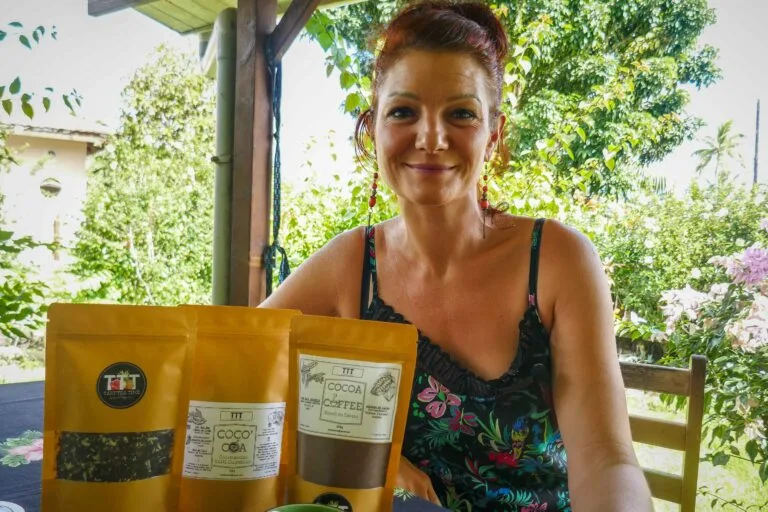 Smiling woman outdoors at a table with three brown packages labeled cocoa/tea in front of her.