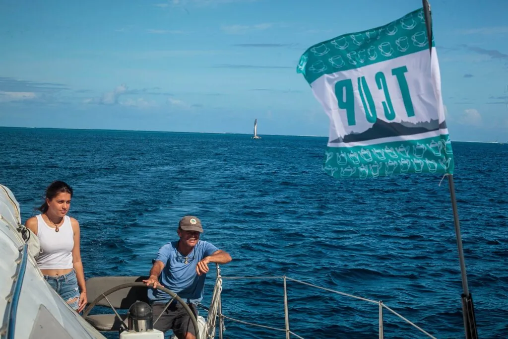 Two People on a Sailboat Steering at Sea, with a Teal Patterned Flag Waving on the Right. Tcupimg_3114-2026 Tcupimg 3114 2026 Régate La T cup Fête Ses 40 Ans